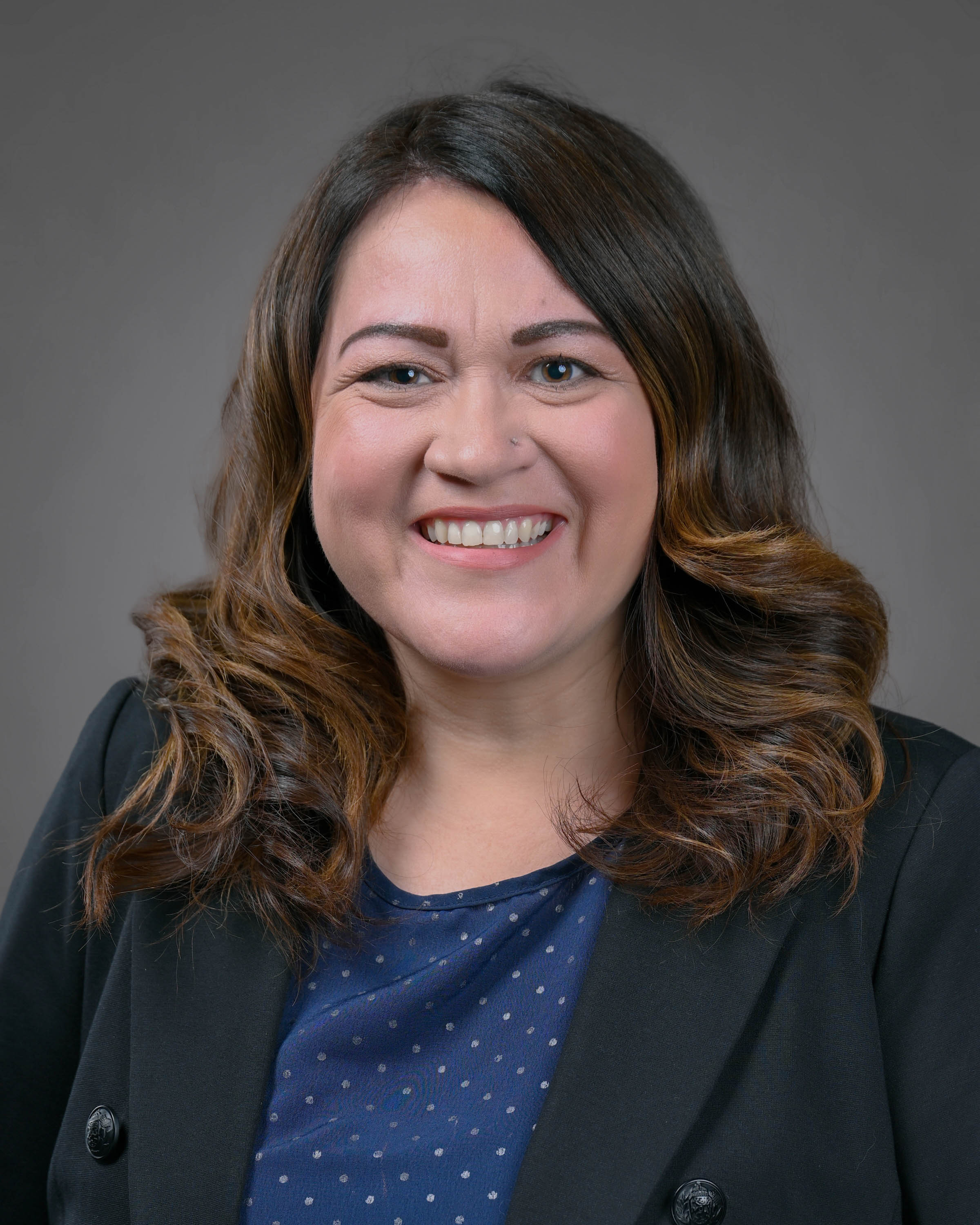 Smiling woman with shoulder length brown hair with curls in a dark suit